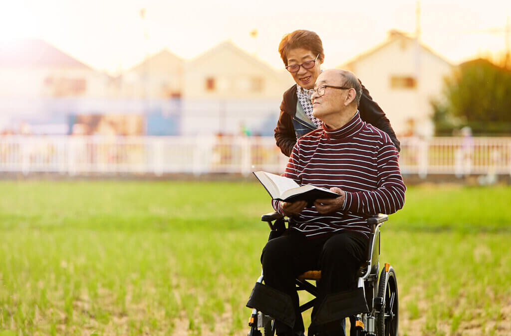 Caregiver burnout: An elderly Asian woman pushes an elderly Asan man in a wheelchair